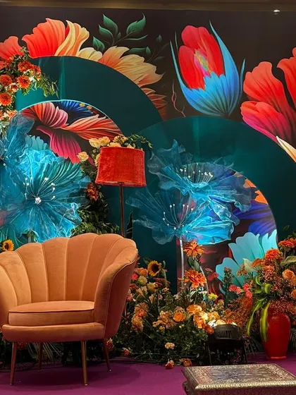 A seating area from the Bhaat ceremony, with a stylish scalloped armchair set against the bold, floral backdrop. The decor is a playful and modern take on traditional celebration design, using color and pattern to create a joyful atmosphere.