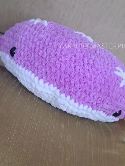 A side view of the purple whale pillow, showing its plump shape and cute little fins. It's perfect for cuddling or as a decorative pillow.
