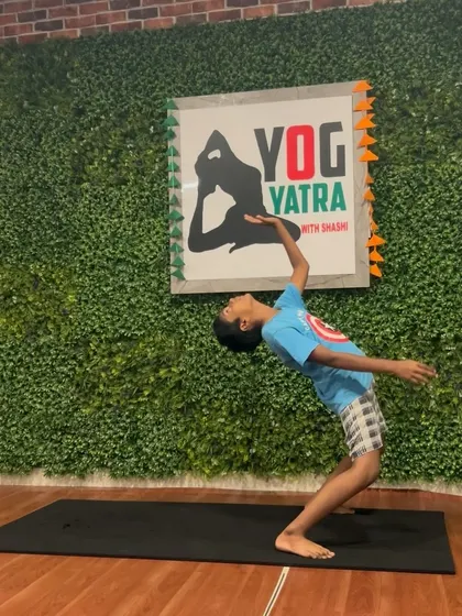 A young boy practices a standing backbend, reaching back with grace and openness.