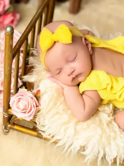 Dressed in a bright yellow outfit, this newborn sleeps on a tiny brass bed. The calendar prop is a great way to commemorate the baby's birth date in the photo.