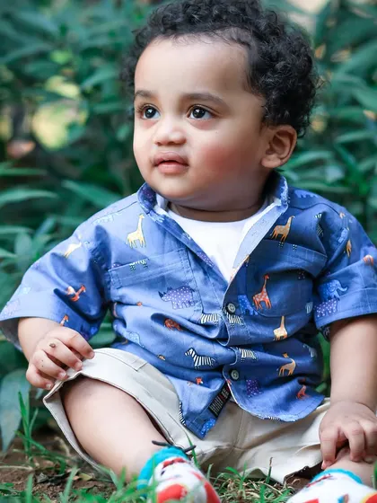 A one-year-old boy, full of curiosity, sits in the grass. His animal-print shirt perfectly complements the natural, wild setting of our outdoor shoot.