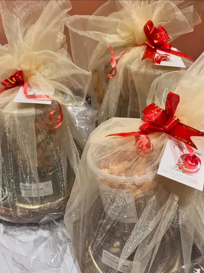 A collection of gift hampers elegantly wrapped in sheer fabric with a bright red ribbon. These custom arrangements can hold jars of cookies, nuts, or small cakes.