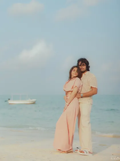 A full-length portrait of the couple standing by the sea, with a boat in the background, adding a touch of local character to their destination shoot.