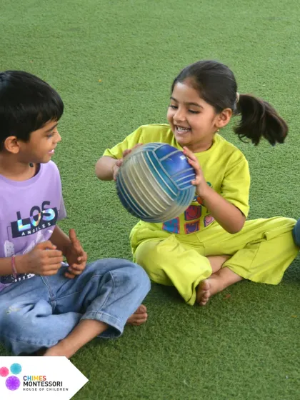 Two children share a ball on the soft turf of our play area, their smiles showing the simple joy of outdoor activity and friendship.