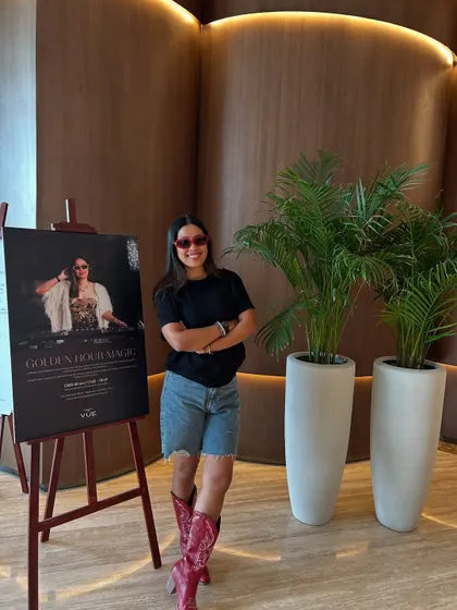 Posing next to my event poster for a 'Golden Hour Magic' session in Oman. This shows the professional branding and promotion for my international residencies.