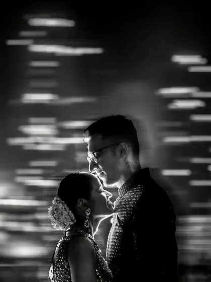 A creative motion-blur portrait in black and white. The moving city lights in the background contrast with the still, intimate moment of the couple.
