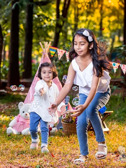 Two sisters playing with bubbles in a park during an outdoor photoshoot. This candid shot captures the carefree joy and fun of sibling playtime.