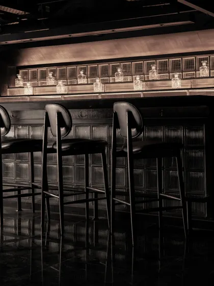 The bar area at Lair, a composition of shadow and minimal light. The design uses focused lighting to highlight the bottles and the dark, fluted bar front, creating a dramatic focal point.
