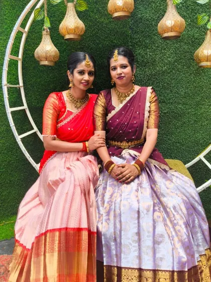 Two clients looking gorgeous in their respective custom half sarees, one in red and pink, the other in wine and lavender.