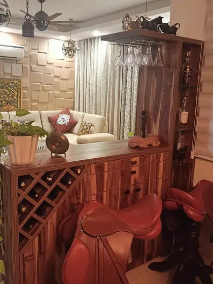 A custom wooden bar unit designed for the Bohemian-themed home. It includes a wine rack, glass holders, and is complemented by unique decor like leather saddles used as bar stools.