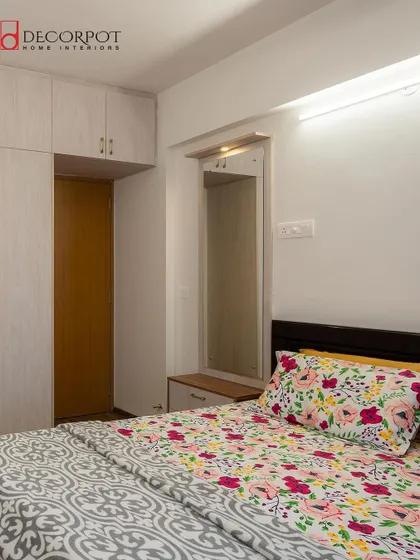 A simple yet charming bedroom with a light wood-finish wardrobe and an integrated dressing table. The floral bedding adds a touch of color and softness to the space.