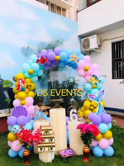 An underwater adventure with this Little Mermaid theme. I used a palette of ocean blues, purples, and yellows to create a balloon arch decorated with character cutouts like Ariel, Flounder, and Sebastian for an outdoor party.