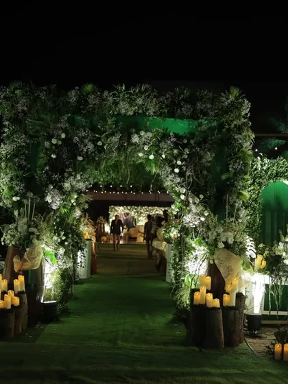 A lush green entrance I designed for an engagement party. The archway is covered in foliage and white flowers, with pillar candles on wooden stumps lighting the path and creating a warm, welcoming ambiance.