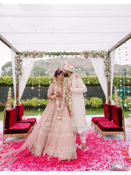 A wide shot of the couple sharing a kiss under their beautiful mandap, covered in flowers.