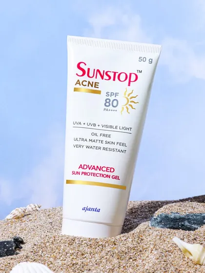 This sunscreen for acne prone skin is shot on a sandy beach with shells. This setting immediately communicates the product's primary function: sun protection in an outdoor environment.