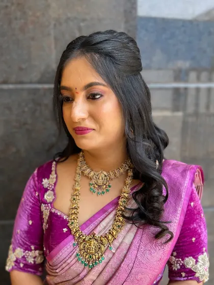 A simple yet elegant party look. The hair is styled in a half-updo with gentle waves, which works beautifully with the client's purple silk saree and temple jewelry.