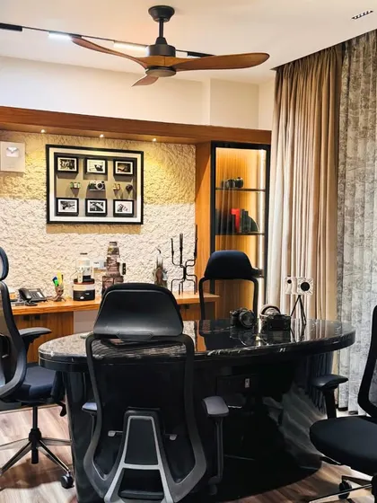 A professional home office or studio space from the Paschim Vihar project. The design includes a large marble-top desk, ergonomic chairs, and custom wood cabinetry with a textured stone accent wall.