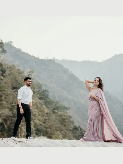 A stunning wide shot from a pre-wedding session in the mountains. The bride's flowing saree against the vast, serene landscape creates a breathtakingly cinematic and romantic image.