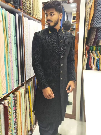 The power of a black sherwani is unmatched. This piece is crafted from a self-patterned jacquard fabric and styled with a matching beaded necklace for a sleek, modern, and elegant groom's look.