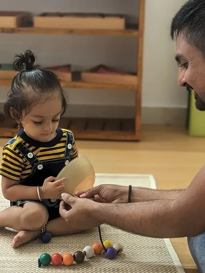 A guide engages with one of our youngest children, exploring a bead threading activity that develops fine motor skills and concentration. Every interaction is an opportunity to build trust and connection, which is the foundation of all learning.