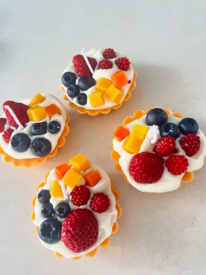 A set of four adorable fruit tart candles, each topped with a variety of wax fruits like strawberries, blueberries, and mango.