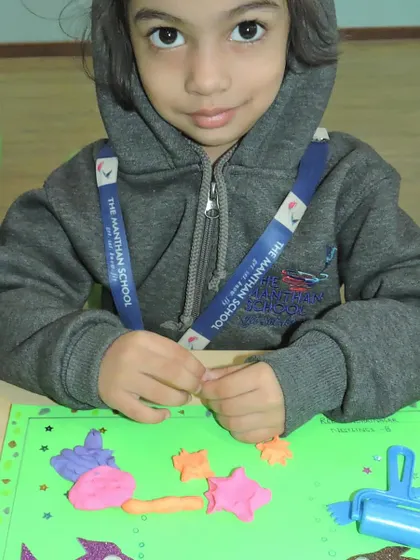 A student shows her colorful clay creation, featuring starfish and other sea elements, as part of the aquatic animals theme.