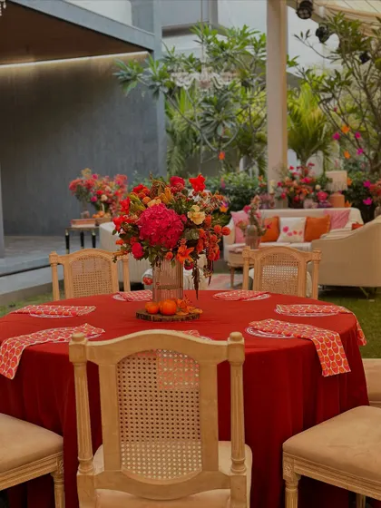 A bold red tablecloth sets the stage for a vibrant centerpiece, creating a striking look in the garden setting.