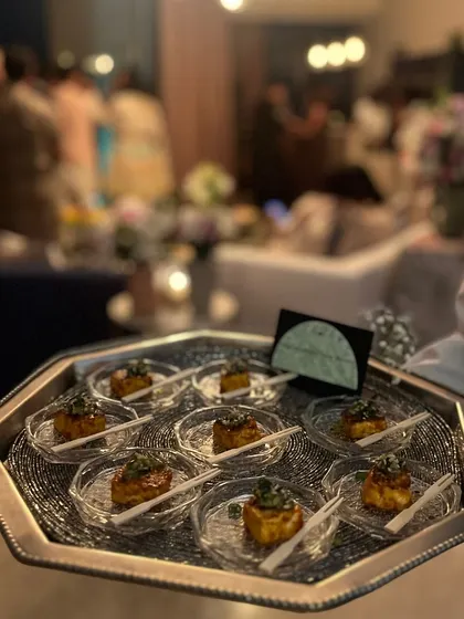 A server presenting a tray of our Jackfruit Kulcha bites at a festive house party. The blurred background of guests enjoying themselves shows how our seamless service integrates into the party atmosphere.