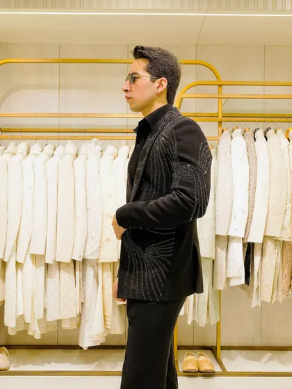 A side profile of the black-on-black outfit, featuring a blazer with delicate, flowing beadwork on the shoulders and lapels. The craftsmanship adds a layer of luxury.