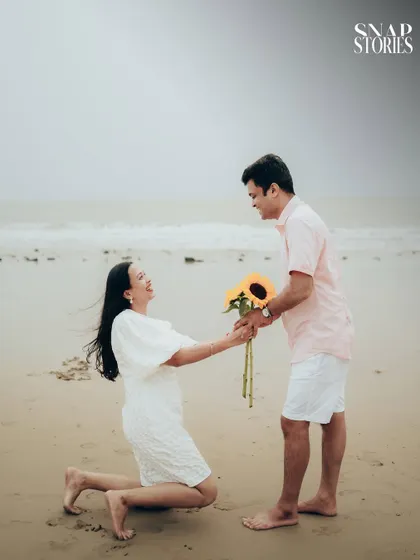 A playful and romantic proposal moment on the sand, with sunflowers adding a bright, cheerful touch to this casual beach pre-wedding shoot.