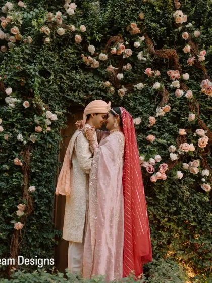 A couple shares an intimate moment against a living wall of greenery and soft pink roses. I design these backdrops to serve as beautiful, natural settings for wedding portraits.