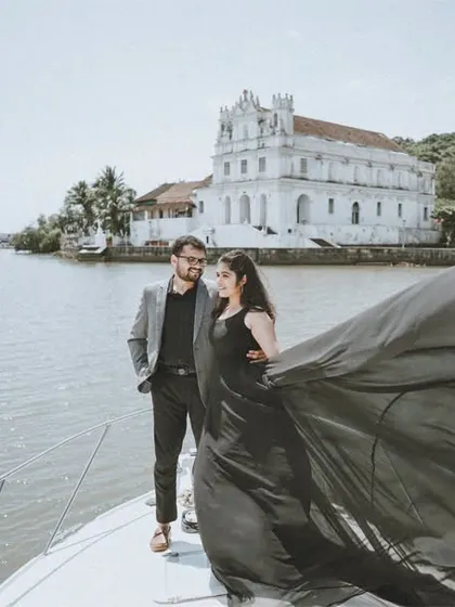 An elegant pre-wedding portrait on a yacht in Goa, capturing the couple against the beautiful backdrop of the water and a classic white church.