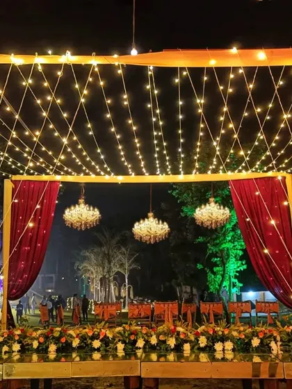 A magical outdoor dining setup for a reception. The canopy of fairy lights and hanging chandeliers creates a starlit sky effect, providing a romantic and enchanting atmosphere for the evening.