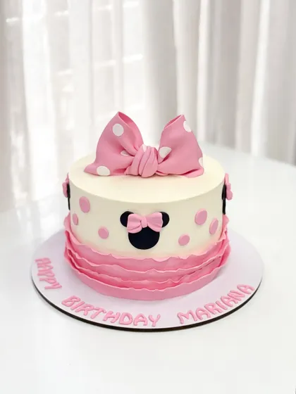 A sweet and classic Minnie Mouse cake for Mariana's birthday. The design features Minnie's iconic silhouette, a big pink bow, and pretty pink ruffles.
