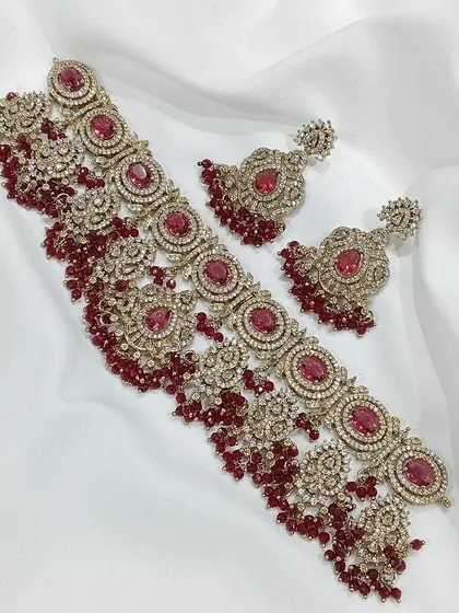 This choker set is available in multiple colors including ruby, emerald, and grey. The intricate metalwork combined with colored stones and pearl or bead droppings offers a sophisticated and royal look.