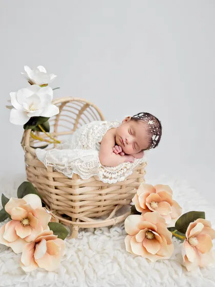 A wider shot of the floral bassinet setup, showing the baby surrounded by beautiful peach and white magnolias.