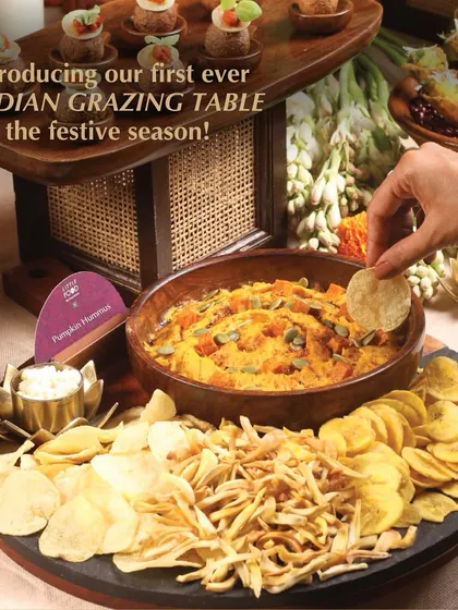 A guest enjoying our Indian grazing table, dipping a banana chip into our flavorful pumpkin hummus. This shot captures the interactive and enjoyable nature of our grazing spreads.