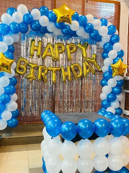 A classic birthday cake-cutting setup with a blue and white balloon arch and a balloon-covered table.