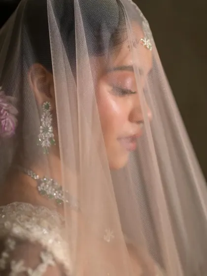 A dreamy close-up through the veil. The soft pink and white tones of her lehenga are complemented by the subtle, clean, and natural makeup.