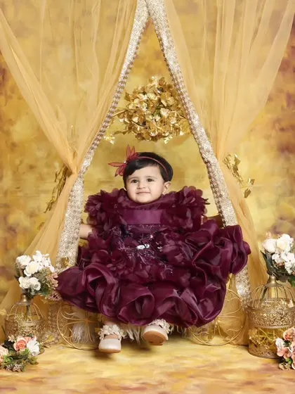A royal portrait for a little princess. This opulent setup features a grand golden swing, a rich purple gown, and floral arrangements, creating a fairy tale image for a special occasion.