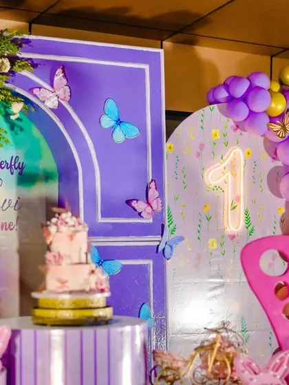 The full view of Hyndhavi's enchanting butterfly-themed first birthday party. The setup combines a rich purple backdrop with soft floral elements and fluttering butterflies for a truly magical effect.