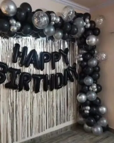 A stylish black and silver balloon frame with a fringe curtain, perfect for a modern birthday celebration at home.