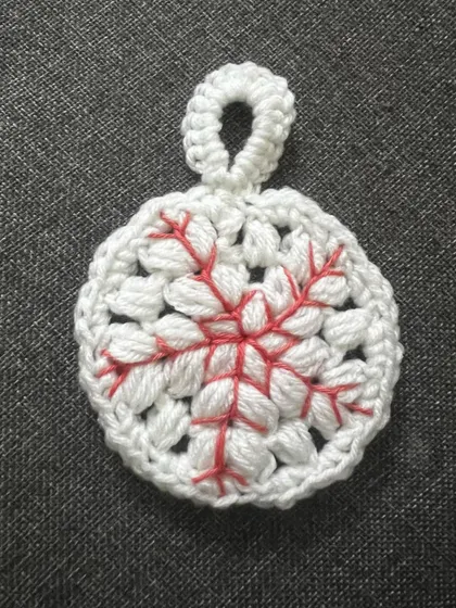 A close-up of my white snowflake ornament with red embroidered details. This design adds a lovely pop of color and intricate detail to your Christmas tree.