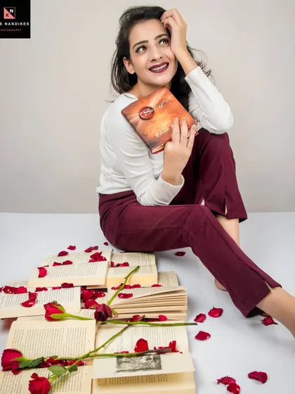 A seated portrait from the 'Bittersweet Memories' series. The model holds a book, surrounded by torn pages and roses, her pose suggesting a moment of sad reflection.