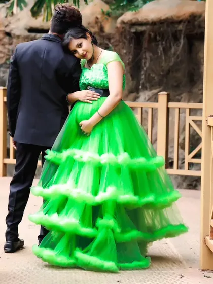 A romantic pose of an expecting couple on a bridge, with the woman in a lime green gown resting her head on her partner's shoulder.