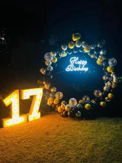 A striking outdoor nighttime setup for a 17th birthday, with a circular balloon frame, neon sign, and large marquee numbers on the grass.
