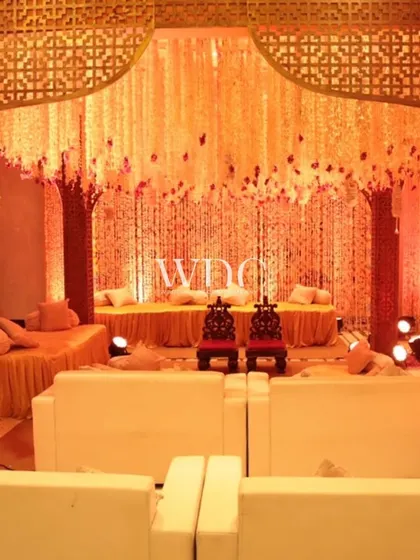 A beautiful and traditional seating area, featuring a backdrop of cascading floral strings and low seating with bolsters, all in a warm, golden-orange hue.