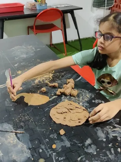 A young girl is completely absorbed in her clay painting. This form of sensory art allows children to connect with the material in a fluid, expressive way, blending painting and sculpting.