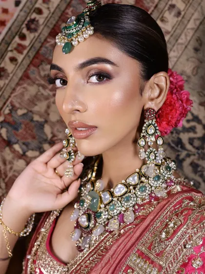 A close-up portrait highlighting the intense bronze eye makeup and the intricate details of the multi-layered polki and emerald necklace.