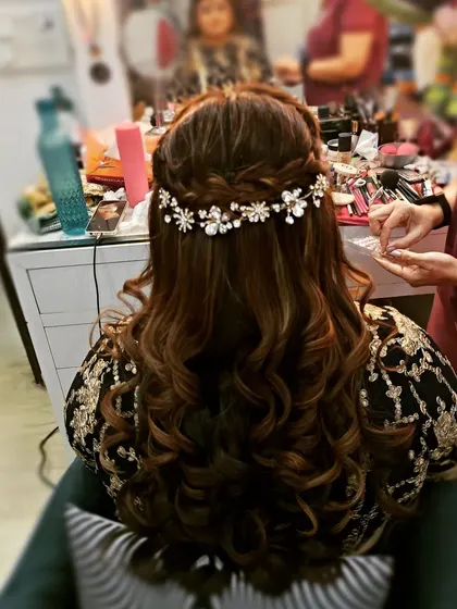 A half-up hairstyle with a crown braid and soft waves, finished with a jeweled floral accessory. This is a beautiful and intricate look for a special occasion.